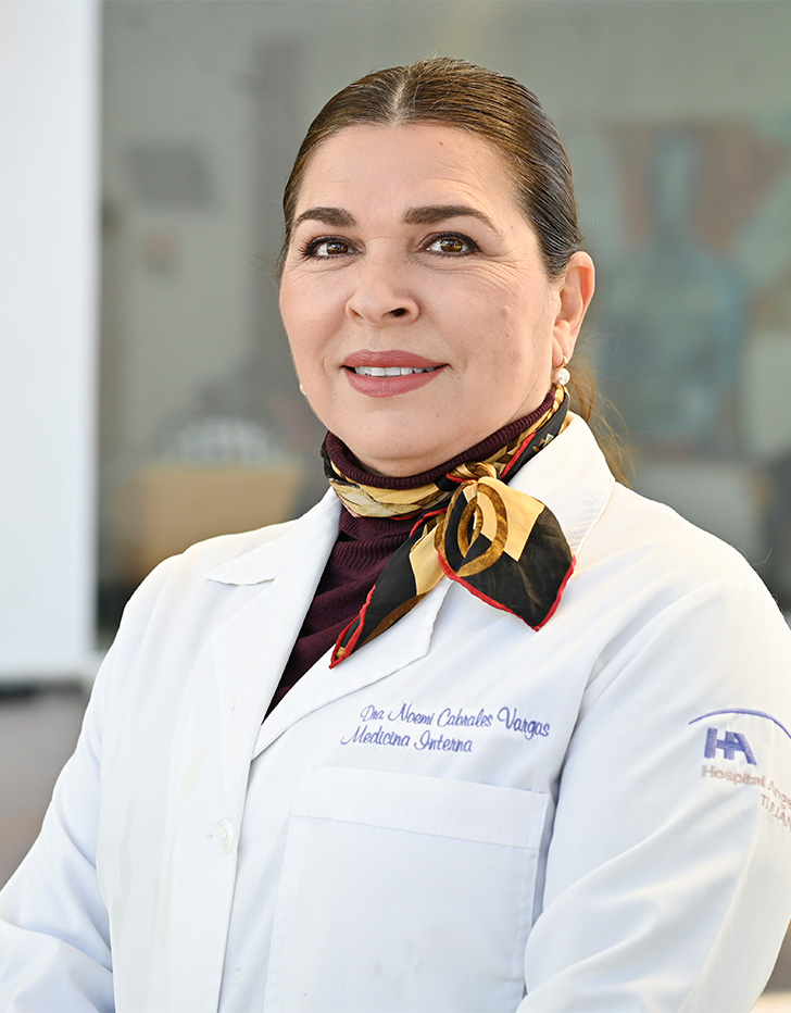 Es la foto de perfil de una médica internista en Tijuana de Hospital Angeles. Usa una bata blanca con una pañoleta color vino con amarillo. Está de perfil y está sonriendo ligeramente.