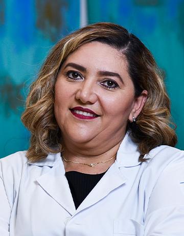 Es la foto de perfil de un ginecólogo en Villahermosa de Hospital Angeles. Usa una bata nlanca con una blusa negra. Tiene el cabello corto color café claro. Usa un labial rojo. Está sonriendo.
