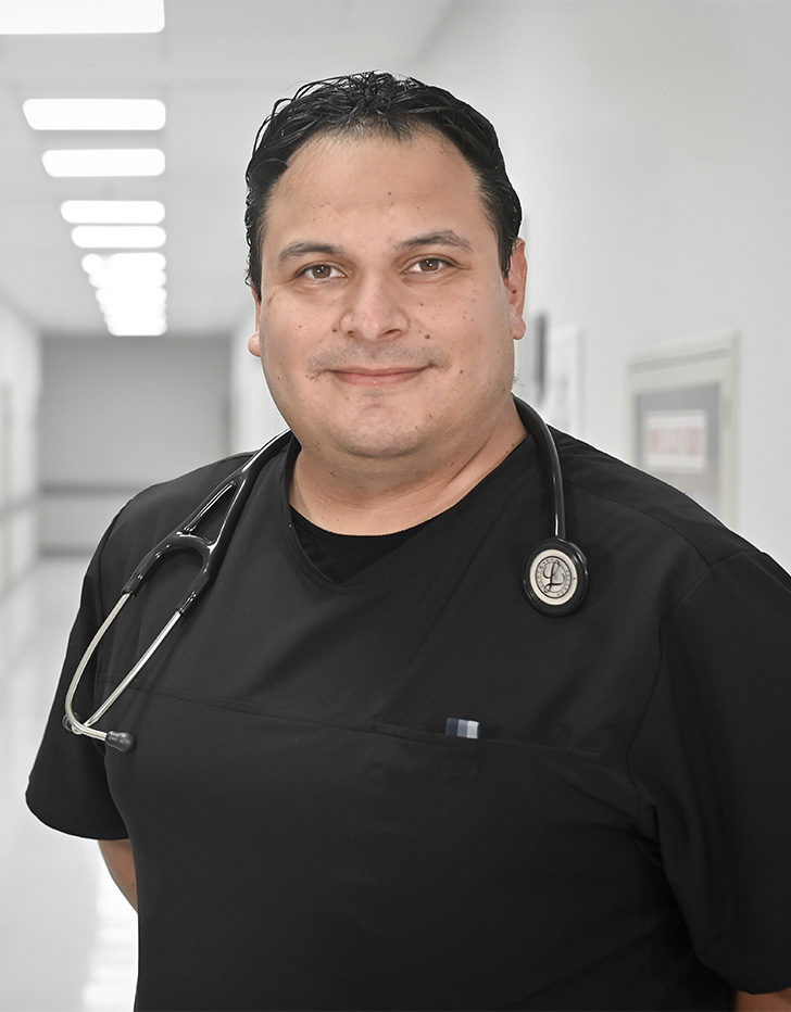 Es la foto de perfil de un médico internista, cardiólogo intervencionista y cardiólogo en Ciudad de México de Hospital Angeles Universidad.  Usa un uniforme médico negro con un estetoscopio en el cuello. Tiene el cabello negro y los brazos cruzados por detrás. Está sonriendo.