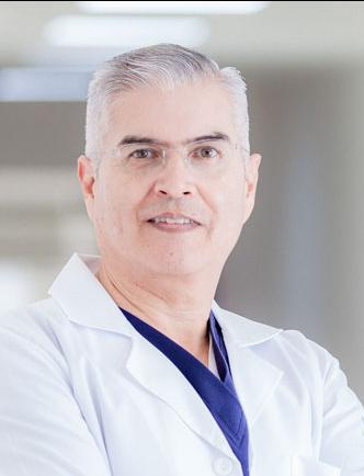 Es la foto de perfil de un ginecólogo en San Luis Potosí de Hospital Angeles. Usa una bata blanca con un uniforme médico azul. Tiene el cabello gris. Está sonriendo.