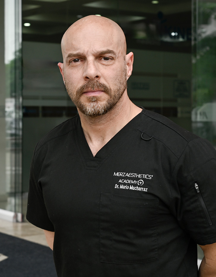 Es la foto de perfil de un cirujano plástico en Villahermosa de Hospital Angeles. Usa un uniforme médico negro. Tiene los brazos cruzados por detrás. Tiene barba. Está serio.