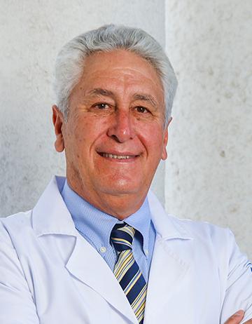 Es la foto de perfil de un urólogo en León de Hospital Angeles León. Utiliza una bata blanca, tiene camisa azul claro y corbata. Tiene los brazos cruzados.