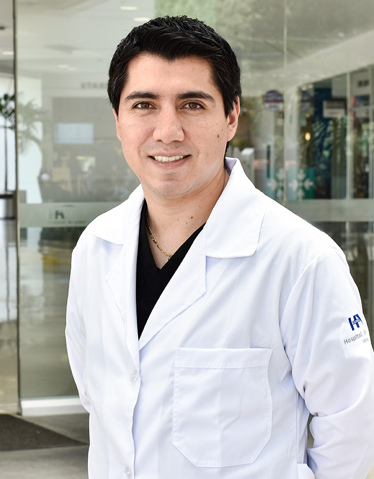 Es la foto de perfil de un ortopedista y traumatólogo en Ciudad de México de Hospital Angeles Acoxpa. Usa una bata blanca con un uniforme médico color azul oscuro y una cadena dorada. Tiene el cabello negro y ojos cafés.