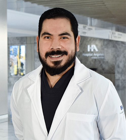 Es la foto de perfil de un cirujano general en Querétaro de Hospital Angeles Centro-sur. Usa una bata blanca con un uniforme médico color negro. Tiene barba tupida y cabello color negro. Está sonriendo.