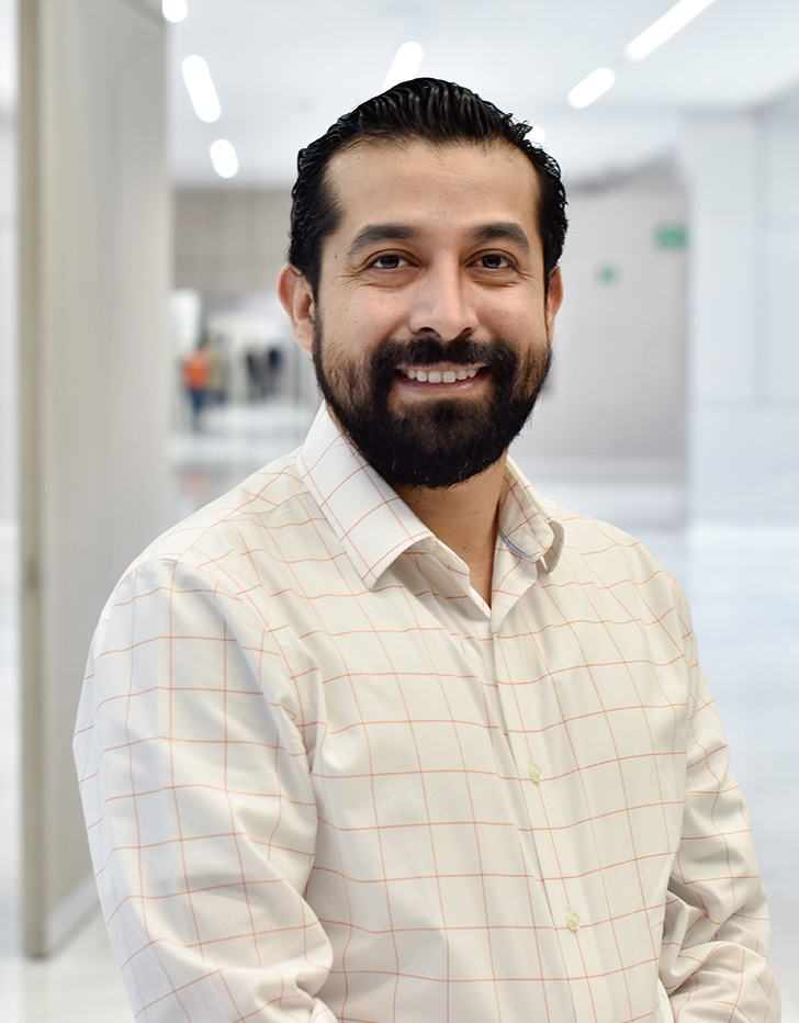 Es la foto de perfil de un reumatólogo en Querétaro de Hospital Angeles Centro Sur. El doctor viste una camisa blanca con líneas que forman cuadros tiene barba. 