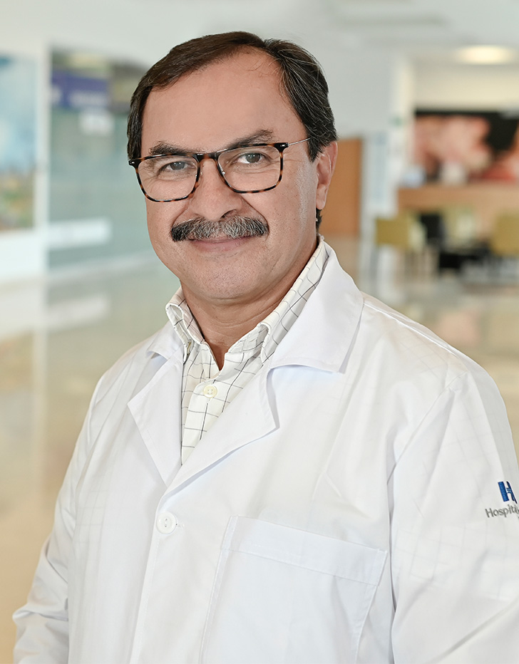 Es la foto de perfil de un cirujano general en Xalapa de Hospital Angeles. Usa una bata blanca con una camisa verde. Tiene el cabello negro y el bigote gris. Está sonriendo.