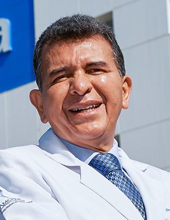 Es la foto de perfil de un cirujano plástico en Ciudad de México de Hospital Angeles Lindavista. Tiene el cabello gris. Usa una bata blanca, una camisa azul claro y una corbata azul más oscuro. Está sonriendo.