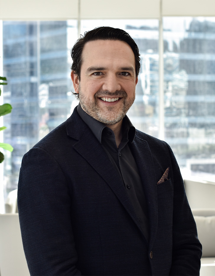 Es la foto de perfil de un cirujano plástico en San Pedro Garza de Hospital Angeles Valle Oriente. Usa un saco negro con una camisa negra. Tiene el cabello y barba negra. Está sonriendo.