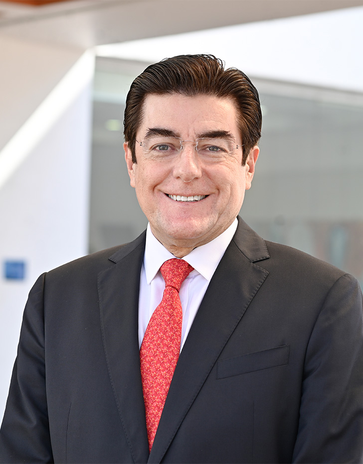 Es la foto de perfil de un cardiólogo en Tijuana de Hospital Angeles Tijuana. Usa un saco negro con una camisa blanca y una corbata roja. Tiene el cabello negro y está sonriendo.