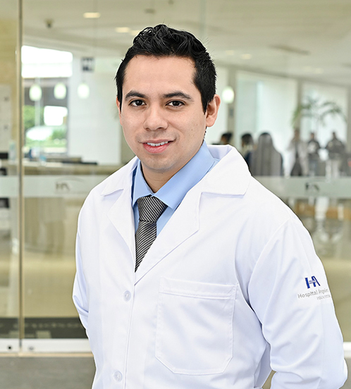 Especialista en Angiología y Cirugía Vascular del Hospital Angeles Acoxpa Ciudad de México. Usa un abata blanca y una camisa azul con corbata. Tiene el cabello negro y está sonriendo.