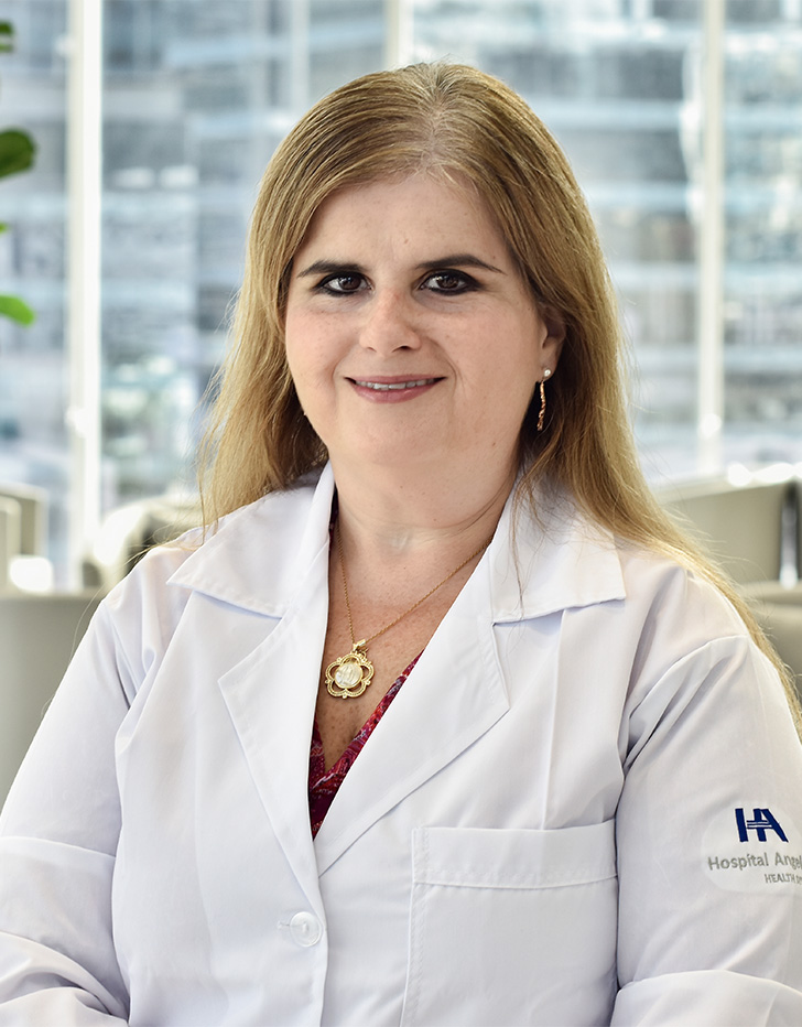 Es la foto de perfil de una gastroenteróloga pediátrica en San Pedro Garza de Hospital Angeles Valle Oriente. Usa una bata blanca y un collar dorado. Tiene el cabello largo, lacio y güero. Está sonriendo ligeramente.