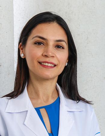 Es la foto de perfil de una oftalmóloga en León de Hospital Angeles León. Usa una bata blanca con una blusa azul, unos aretes blancos y lleva labial rojo.