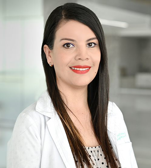 Es la foto de perfil de una angióloga y cirujana vascular y endovascular en Querétaro de Hospital Angeles Centro Sur. La doctora tiene una bata blanca una blusa beige con puntos negros y el cabello lacio.