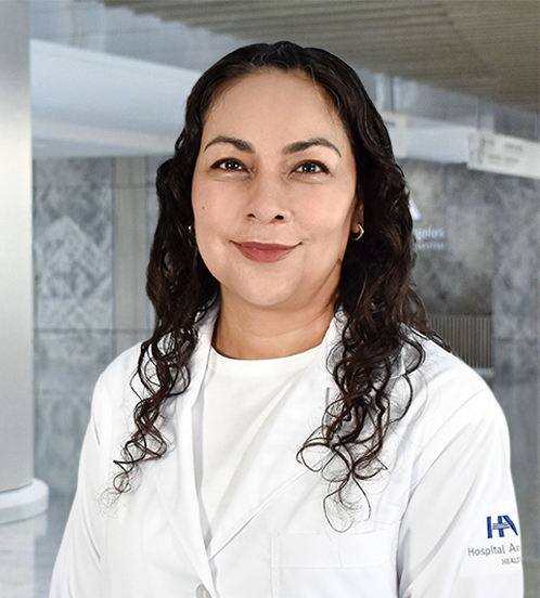 Es la foto de perfil de una pediatra en Querétaro de Hospital Angeles Centro-sur. Usa una playera blanca con una bata blanca de Hospital Angeles. Tiene el cabello chino, corto y café.