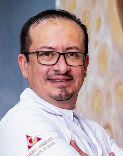 Es la foto de perfil de un nefrólogo en León de Hospital Angeles León. Usa una bata blanca, tiene los brazos cruzados, usa lentes cuadrados y está sonriendo.