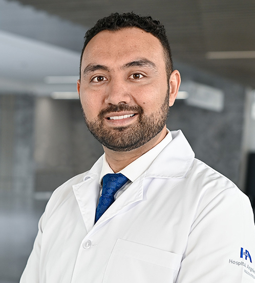 Es la foto de perfil de un biólogo de la reproducción en Querétaro de Hospital Angeles Centro-sur. Usa una camisa y bata blanca con una corbata azul. Tiene barba y cabello color café oscuro.
