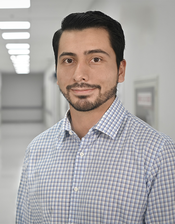 Es la foto de perfil de un urólogo en Ciudad de México de Hospital Angeles Universidad. Usa una blusa blanca con cuadros. Tiene el cabello y barba negra. Está sonriendo ligeramente.