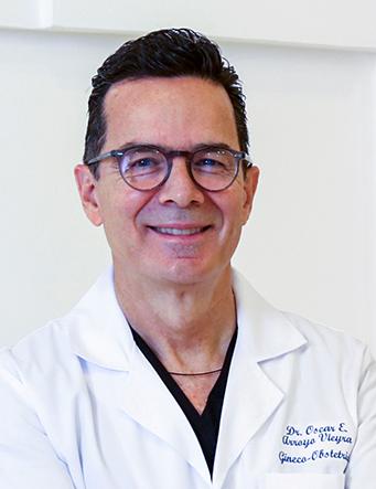 Es la foto de perfil de un ginecólogo y obstetra en León de Hospital Angeles León. Usa una bata blanca con camisa negra en cuello V. Usa lentes negros.