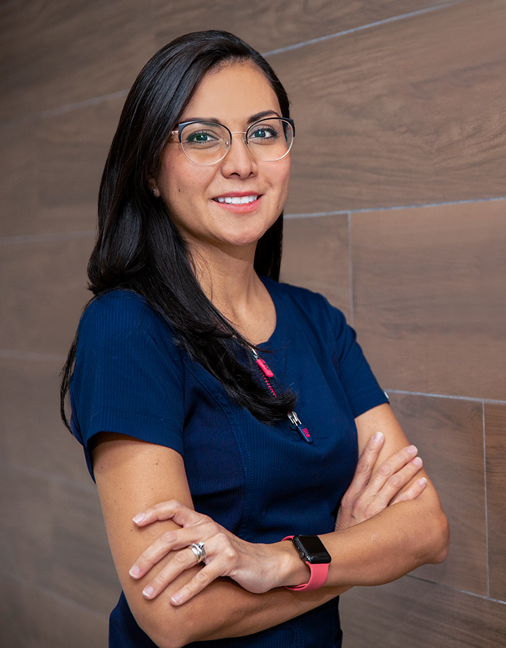 Es la foto de perfil de una otorrinolaringóloga y cirujana general en Ciudad de México de Hospital Angeles Santa Mónica. Usa un uniforme médico azul. Tiene el cabello largo y lacio. Usa lentes y tiene los brazos cruzados.