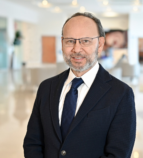 Es la foto de perfil de un pediatra y cirujano pediátrico en Xalapa de Hospital Angeles Xalapa. Usa un uniforme médico azul con negro. Tiene el cabello café y barba gris. Usa lentes.