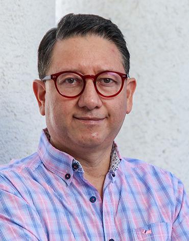 Es la foto de perfil de un neumólogo especialista en broncoscopía en León de Hospital Angeles León. Utiliza una camisa rosa con azul. Tiene lentes con marco rojo. 