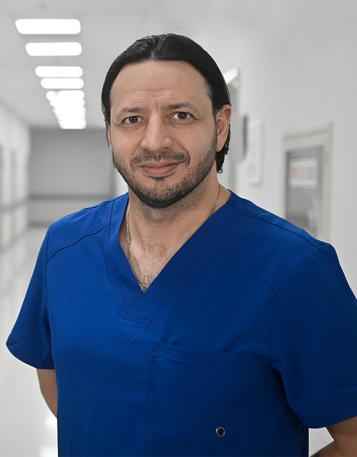 Es la foto de perfil de un pediatra en Ciudad de México de Hospital Angeles Universidad. Usa un uniforme médico azul. Tiene el cabello y barba negra. Tiene los brazos cruzados en la parte de atrás.
