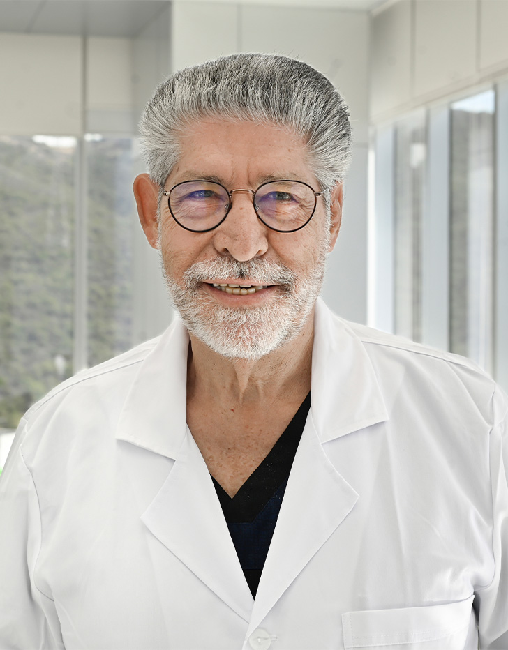 Es la foto de perfil de un ginecólogo y obstetra en San Pedro Garza de Hospital Angeles Valle Oriente. Usa una bata blanca con un uniforme médico azul marino. Tiene el cabello y barba canoso. Usa lentes.