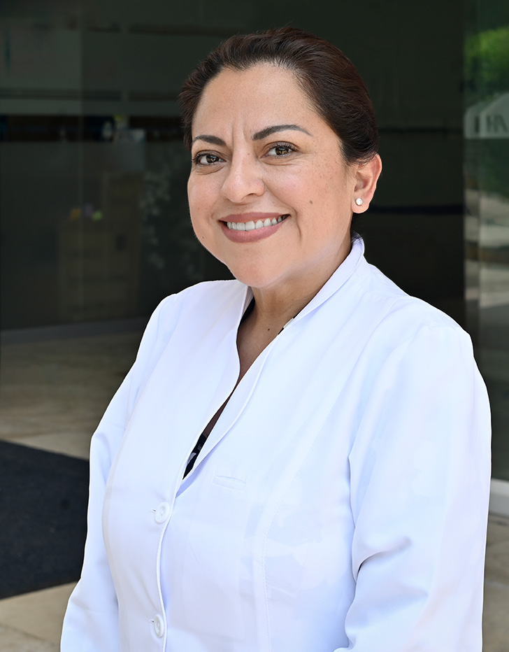 Es la foto de perfil de una oncóloga médica pediátrica en Villahermosa de Hospital Angeles Villahermosa. Usa una bata blanca. Tiene el cabello café y recogido. Está sonriendo y de perfil.