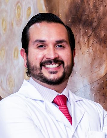 Es la foto de perfil de un especialista en radioterapia en León de Hospital Angeles León. Utiliza una bata blanca, camisa clara y corbata roja.