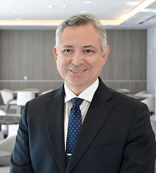 Es la foto de perfil de un cirujano general en San Pedro Garza de Hospital Angeles Valle Oriente. Usa un saco negro con una camisa blanca y corbata azul. Tiene el cabello gris. Está sonriendo.