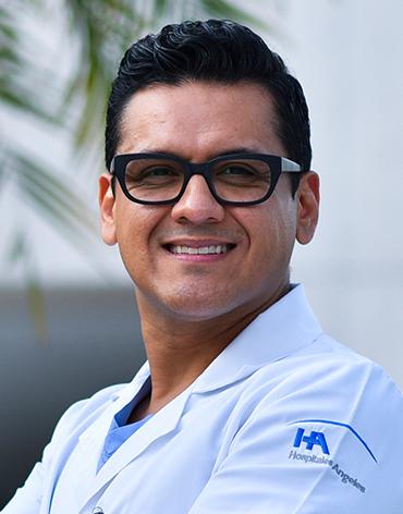 Es la foto de perfil de un cirujano general en Villahermosa de Hospital Angeles Villahermosa. Usa una bata blanca con un uniforme médico azul. Tiene el cabello negro y usa lentes. Está sonriendo.