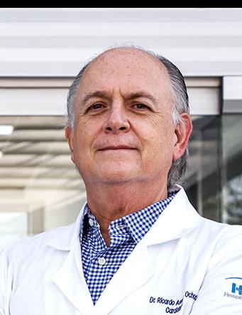 Es la foto de perfil de un cardiólogo en Guadalajara de Hospital Angeles Del Carmen. Utiliza una bata blanca y camisa de cuadros azul con blanco.