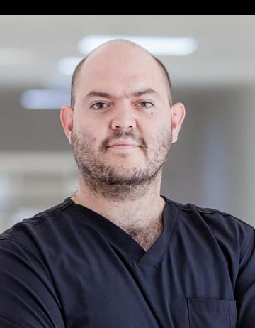 Es la foto de perfil de un ortopedista y traumatólogo en San Luis Potosí de Hospital Angeles San Luis Potosí. Usa un uniforme médico negro. Es calvo y tiene barba razurada. Está sonriendo ligeramente.
