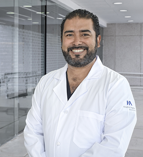 Es la foto de perfil de un pediatra en Villahermosa de Hospital Angeles Villahermosa. Usa una bata blanca con un uniforme médico verde. Tiene el cabello negro. Está sonriendo.