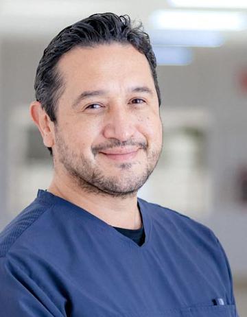 Es la foto de perfil de un ginecólogo y obstetra en San Luis Potosí de Hospital Angeles San Luis Potosí. Usa un uniforme médico azul marino. Tiene el cabello y barba negro. Está sonriendo ligeramente.