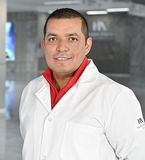 Es la foto de perfil de un gastroenterólogo en Querétaro de Hospital Angeles Centro-sur. Usa una bata blanca con una chamarra/ camisa color rojo. Tiene el cabello color café.