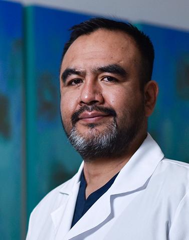 Es la foto de perfil de un psiquiatra en Villahermosa de Hospital Angeles Villahermosa. Usa una bata blanca con un uniforme médico azul. Tiene el cabello y barba negra.