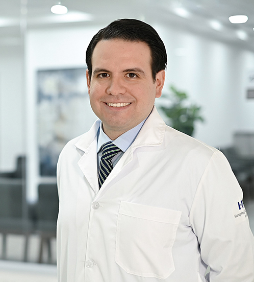 Especialista en Medicina Interna del Hospital Angeles Acoxpa Ciudad de México. Usa una bata blanca, una camisa azul claro y una corbata de rayas azul oscuro con verde. Tiene el cabello negro y está sonriendo.