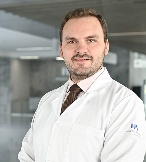Es la foto de perfil de un ortopedista y traumatólogo en Querétaro de Hospital Angeles Centro-sur. Usa una bata blanca con una camisa rosa muy claro y una corbata café. Tiene el cabello y barba castaño.