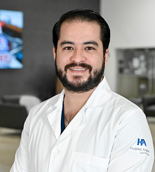 Es la foto de perfil de un cirujano general en San Luis Potosí de Hospital Angeles San Luis Potosí. Usa una bata blanca. Tiene el cabello y barba negra. Tiene los brazos cruzados en la parte baja. Está sonriendo ligeramente.