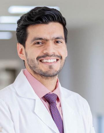 Es la foto de perfil de un reumatólogo en San Luis Potosí. Usa una bata blanca con cxamisa rosa y una corbata morada. Tiene el cabello y barba negra. Está sonriendo.