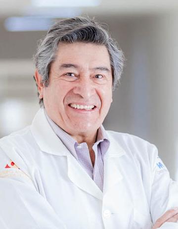 Es la foto de perfil de un dermatólogo en San Luis Potosí de Hospital Angeles San Luis Potosí. Usa una bata blanca con una camisa rosa palo. Tiene el cabello gris. Está sonriendo.