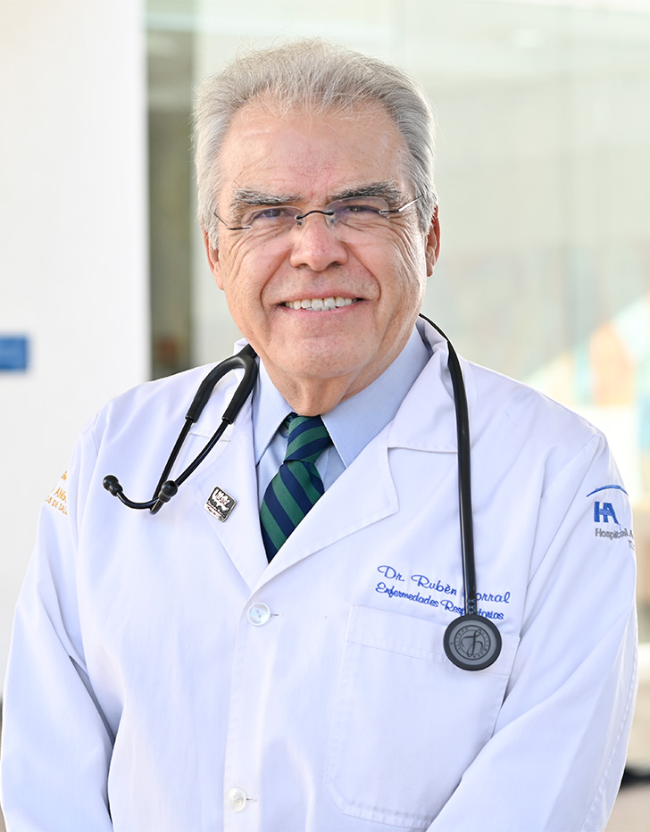 Es la foto de perfil de un neumólogo en Tijuana de Hospital Angeles Tijuana. Usa una bata blanca, camisa azul y corbata verde. Tiene el cabello gris. Está sonriendo.