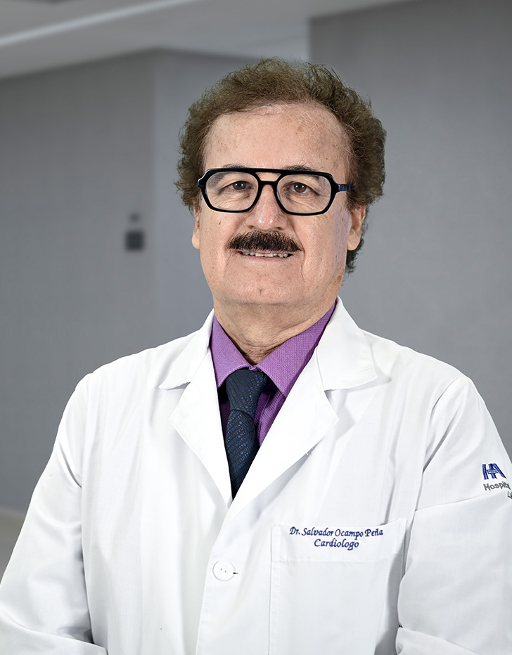 Es la foto de perfil de un cardiólogo en Ciudad de México de Hospital Angeles Lindavista. Tiene el cabello y bigote café. Usa lentes, una bata blanca y una bufanda azul con rojo.