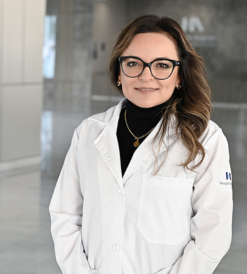 Es la foto de perfil de una ginecóloga y obstetra en Querétaro de Hospital Angeles Centro Sur. La doctora usa una bata blanca, lentes cuadrados negros y joyería dorada.