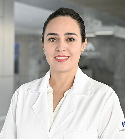 Es la foto de perfil de una oftalmóloga en Querétaro de Hospital Angeles Centro-sur. Usa el cabello recogido con unos aretes plata, una blusa blanca y una bata médica blanca. Tiene los ojos y cabello café.