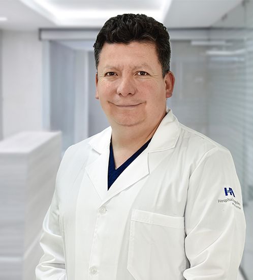 Es la foto de perfil de un cardiólogo en Ciudad de México y Hospital Angeles Universidad. Usa una bata blanca con un uniforme médico azul. Tiene el cabello negro. Está sonriendo.