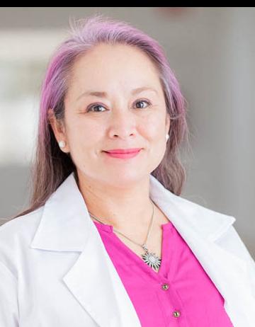 Es la foto de perfil de una dermatóloga en San Luis Potosí de Hospital Angeles San Luis Potosí. Usa una bata blanca y una blusa rosa. Tien el cabello largo y rosa y café. Usa un collar plata con una piedra azul.