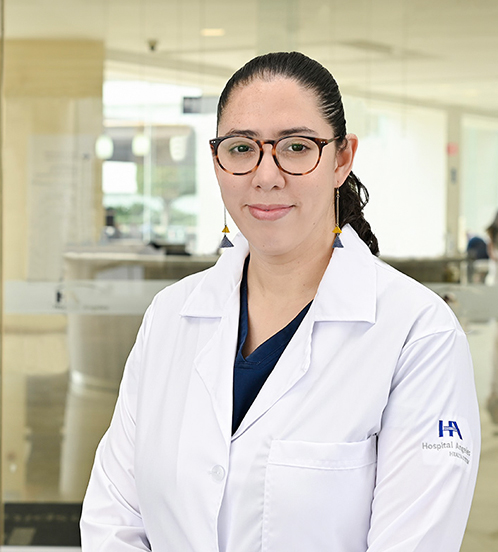 Es la foto de perfil de una gastroenteróloga en Ciudad de México de Hospital Angeles Acoxpa. Usa una bata blanca con un uniforme médico color azul. Usa unos aretes largos con unos triangulos azul y amarillo. Tiene el cabello ondulado y recogido.