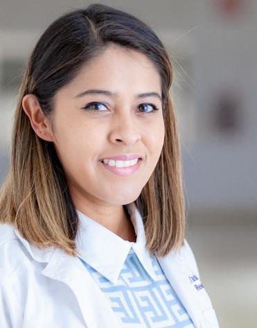 Es la foto de perfil de una reumatóloga en San Luis Potosí de Hospital Angeles San Luis Potosí. Usa una bata blanca con un sueter azul y una camisa blanca. Tiene el cabello corto y castaño. Está sonriendo.